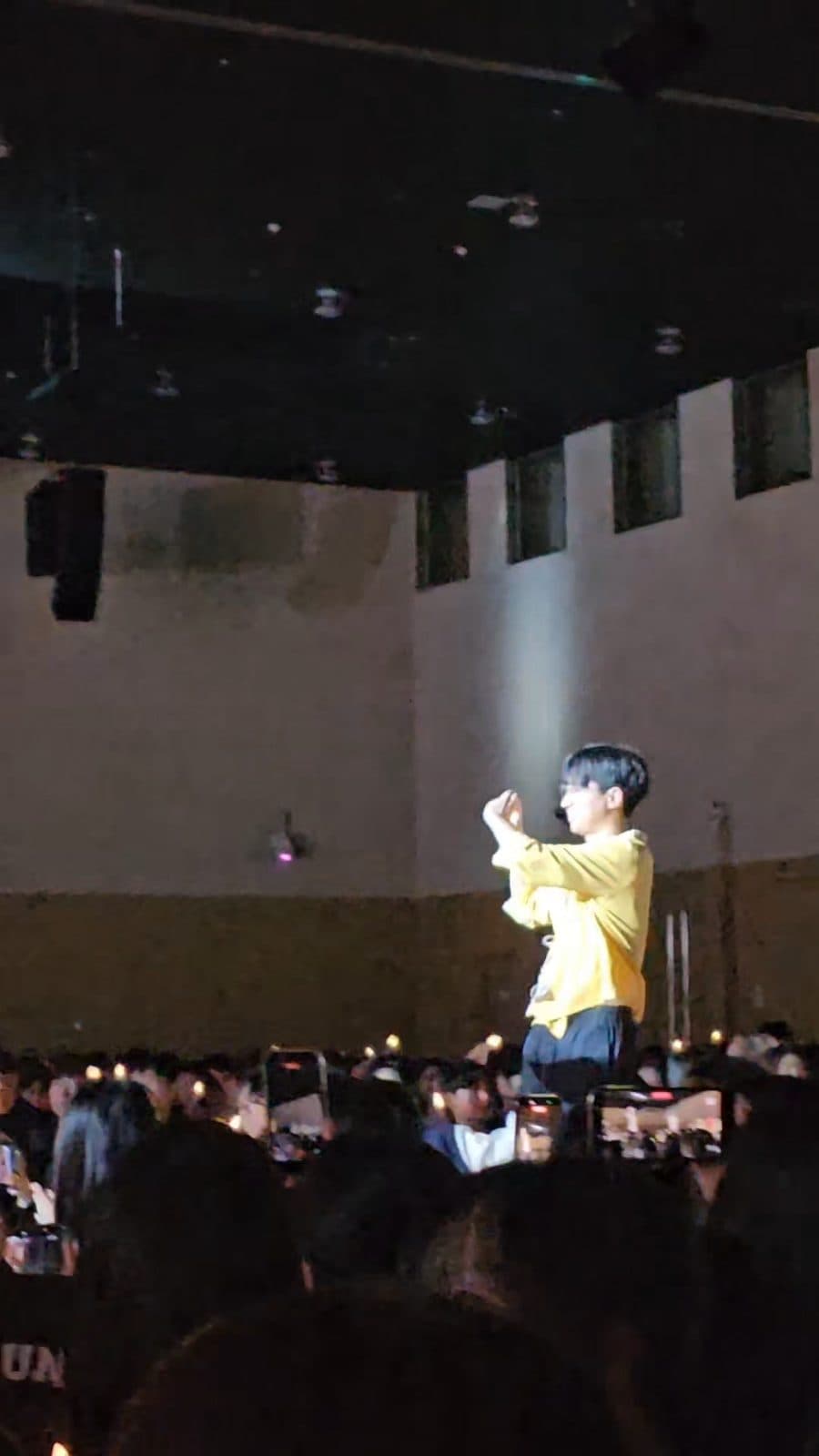 어두운 공연장 무대 위에 노란 단체복 차림의 기획단 구성원이 올라 객석을 향해 서 있고, 관객들이 휴대전화로 촬영하고 있다.