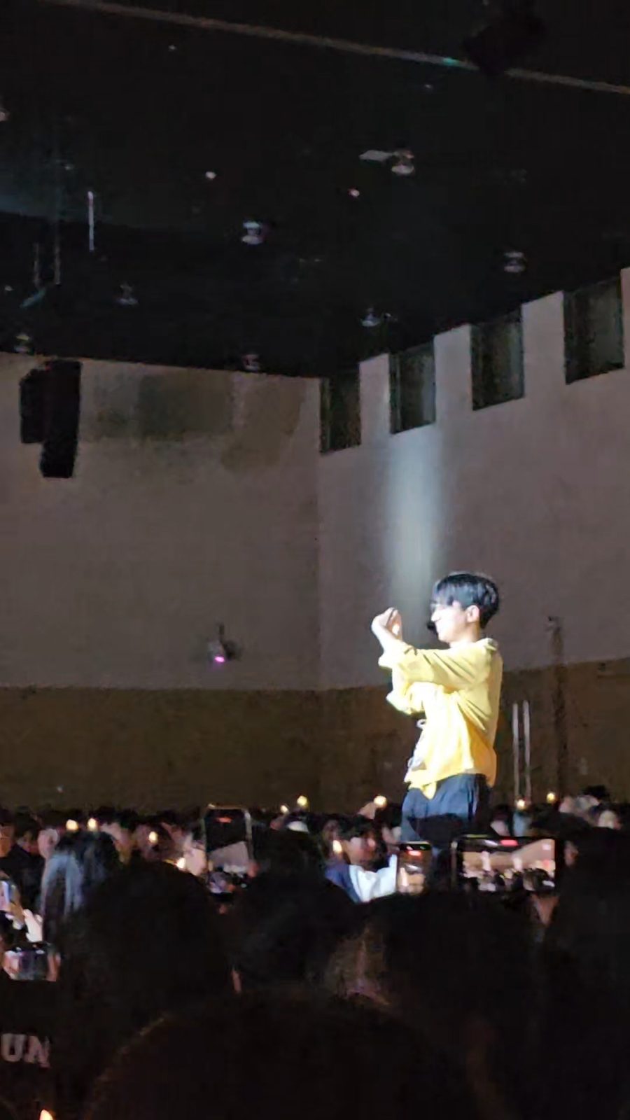 어두운 공연장 무대 위에 노란 단체복 차림의 기획단 구성원이 올라 객석을 향해 서 있고, 관객들이 휴대전화로 촬영하고 있다.